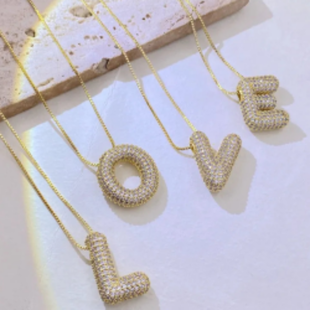Gold necklaces with letter pendants spelling 'LOVE' on a light background